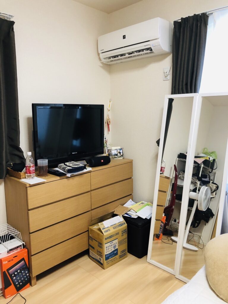 チェストの上にテレビや雑貨、床に段ボールが置かれた片付け前の部屋